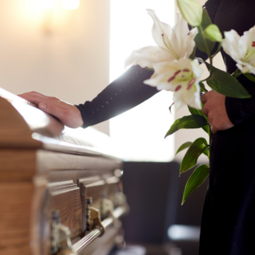 woman holding white lillies at casket at funeral